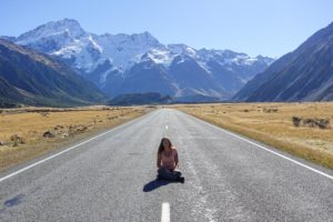 Katy sitzt mitten auf einer verlassenen Straße auf dem Weg zum Mount Cook